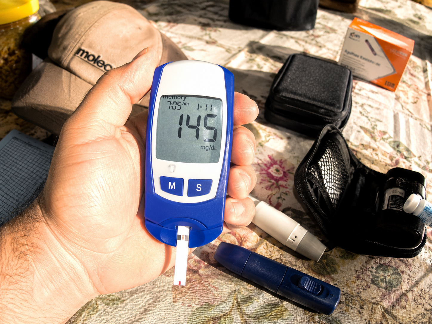 Person holding a glucometer showing 145 mg/dL blood sugar reading
